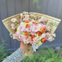 Handheld bouquet of pink, orange, and pale green flowers wrapped in paper