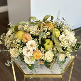Basket of cream roses, ranunculus, and daisies with green apples and ribbon