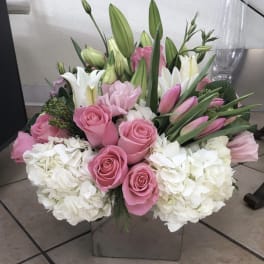Pink roses and white lilies in a square glass vase with white hydrangeas