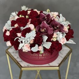 Round box arrangement of red roses, pink spray roses, and purple orchids