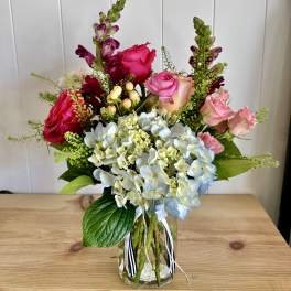 Mixed bouquet of roses, hydrangeas, and snapdragons in a glass vase