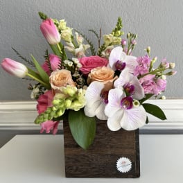 Mixed bouquet in a wooden box with pink tulips, roses, and white orchids