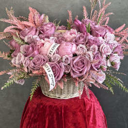 Pink rose arrangement in a wicker basket with ribbon accents