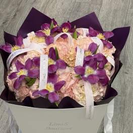 Purple tulips arranged over pale pink hydrangeas in a white box