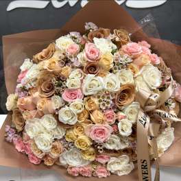 Large bouquet of pastel roses wrapped in brown paper with a satin ribbon