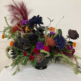 Large mixed floral arrangement in a black vase with dark blooms and dried accents