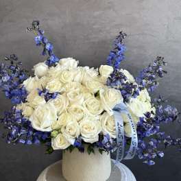 White rose arrangement with blue delphinium in a cream vase