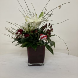 White lilies and red roses in a square glass vase with holiday accents