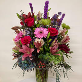 Mixed pink, purple, and green flowers arranged in a glass vase