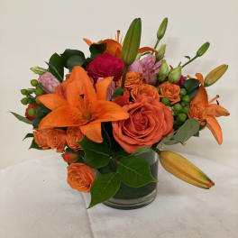 Orange lilies and roses arranged in a glass vase