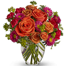 Orange roses and magenta daisies in a clear glass vase