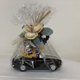 Gift basket wrapped in clear cellophane with flowers and snacks on a black tray