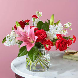 Pink lilies, red roses, and white flowers in a clear glass vase