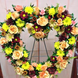Heart-shaped floral wreath with peach roses and bright daisies on a stand