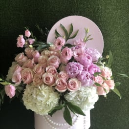 Hatbox arrangement of pink roses, peonies, and white hydrangeas in a pink box trimmed with pearls