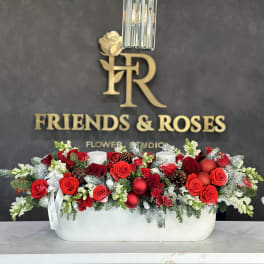 Red rose centerpiece in a white rectangular vase with candles and pinecones