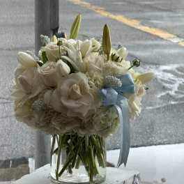 White bouquet in a clear glass vase with a blue ribbon