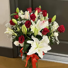Bouquet of red roses and white lilies in a glass vase with a red ribbon