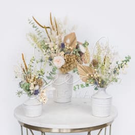Three dried floral arrangements in white vases on a round table