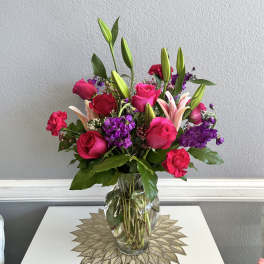 Mixed bouquet of pink roses, lilies, and purple flowers in a clear glass vase