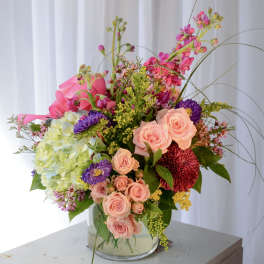 Mixed bouquet in a clear glass vase with pink, peach, purple, and green blooms