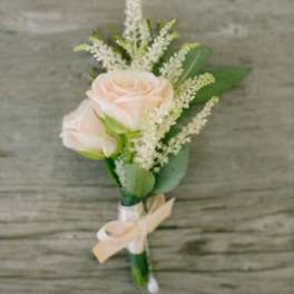 Blush rose wedding boutonniere with white filler flowers and an ivory ribbon bow.