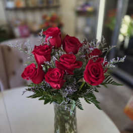 Red roses arranged in a clear glass vase with purple filler flowers