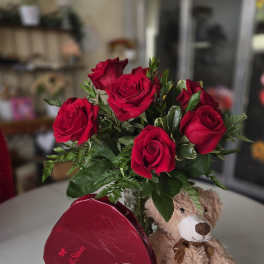 Red roses in a glass vase with a teddy bear and heart-shaped chocolate box