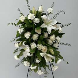 White floral standing spray with lilies, roses, and carnations on a black easel