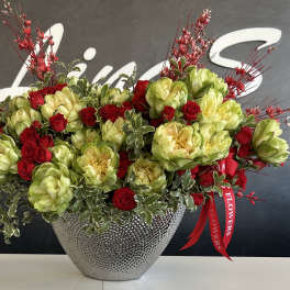 Red roses and green blooms in a silver textured vase with red decorative sprays
