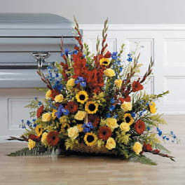 Large red, yellow, and blue sympathy flower arrangement in a basket before a casket