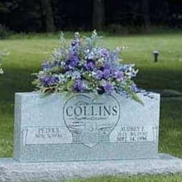 Purple and white mixed flower spray resting on top of a gray granite headstone