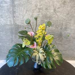 Tropical arrangement with yellow orchids and large monstera leaves in a vase