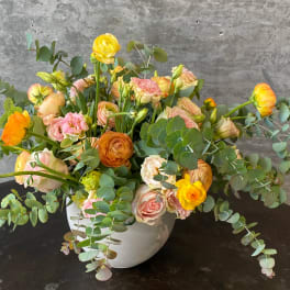 Mixed bouquet of yellow, peach, and pink flowers in a white vase