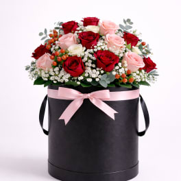 Red and pink roses arranged in a black hatbox with a pink ribbon