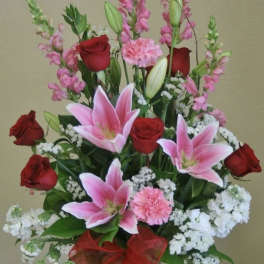 Bouquet of pink lilies and red roses in a glass vase with a red ribbon