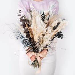 Dried bouquet with beige pampas grass and dark foliage tied with a ribbon