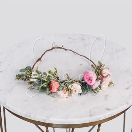 Delicate floral crown with pink and white roses arranged along a vine base on a marble table.