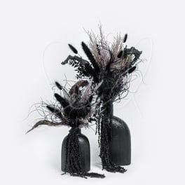 Two black vases hold dark dried floral arrangements.