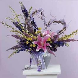 Tall arrangement of pink lilies with purple and yellow flowers in a ribboned vase
