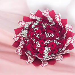 Large bouquet of deep red roses with white filler blooms wrapped in red and patterned paper