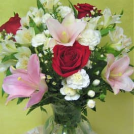 Bouquet of red roses, pink lilies, and white flowers in a glass vase