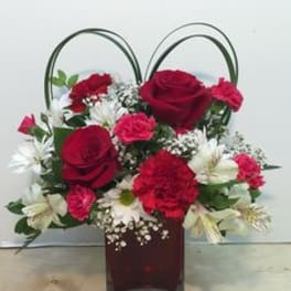 Red roses and carnations in a square glass vase with looped handles