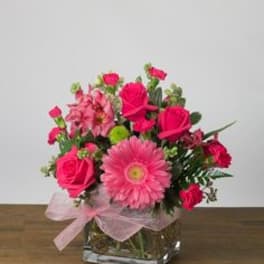 Pink mixed flower arrangement in a square glass vase with a ribbon