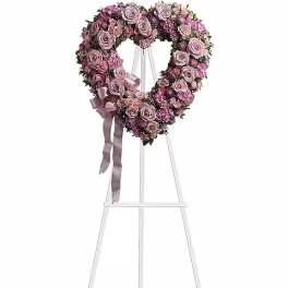 Heart-shaped pink rose wreath on a white stand with ribbon