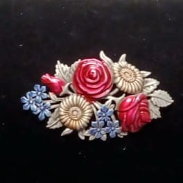Decorative floral brooch with red, cream, and blue flowers on a black background