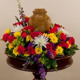 Colorful mixed flower arrangement around a brown urn on a pedestal