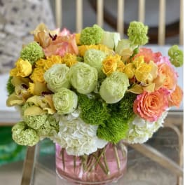 Bouquet of yellow, peach, and green flowers in a pink glass vase