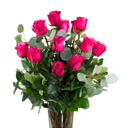 Tall arrangement of bright pink roses with lush foliage in a clear glass vase