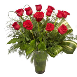 Red roses arranged in a clear glass vase with greenery